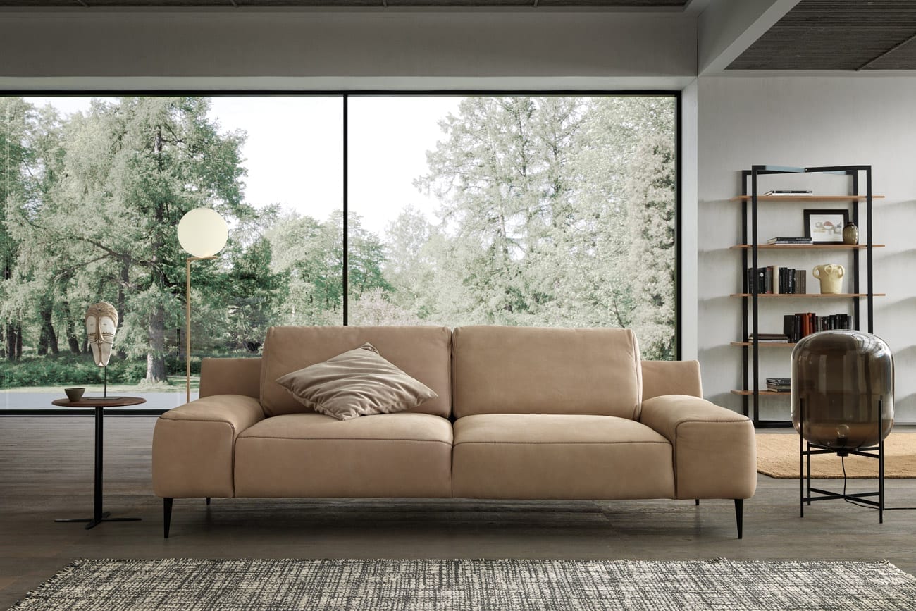 Wohnambiente mit dem 3er-Sofa des Modells Forma mit beigem Lederbezug, Kontrastnaht, Wurfkissen und mattschwarzen Füssen