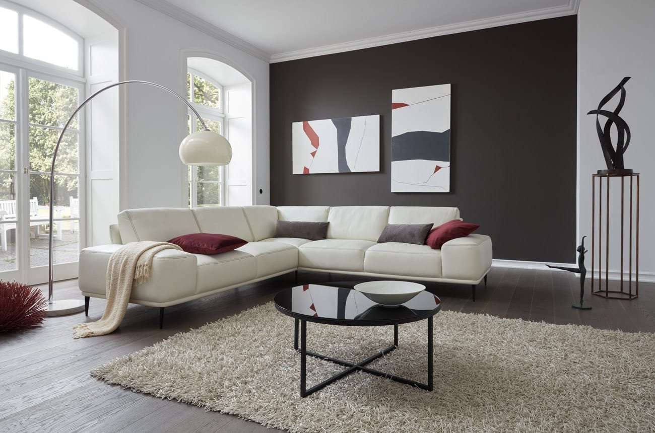 Wohnambiente mit einer Sofakombination des Modells Oslo mit weissem Lederbezug, Wurfkissen, Nierenkissen und mattschwarzen Füssen