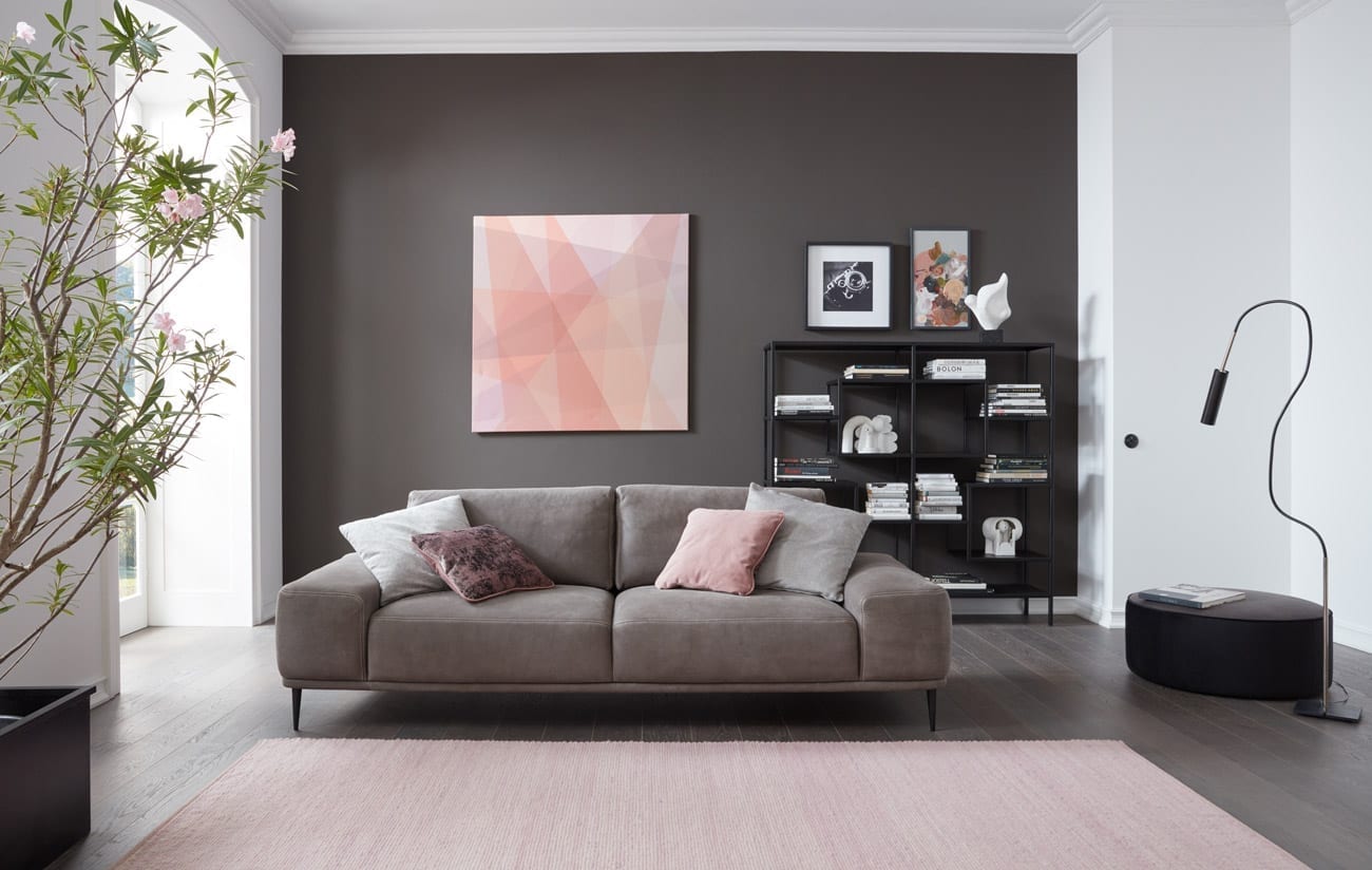 Wohnambiente mit dem 3er-Sofa des Modells Oslo mit braunem Lederbezug, Wurfkissen, Reversekissen und mattschwarzen Füssen