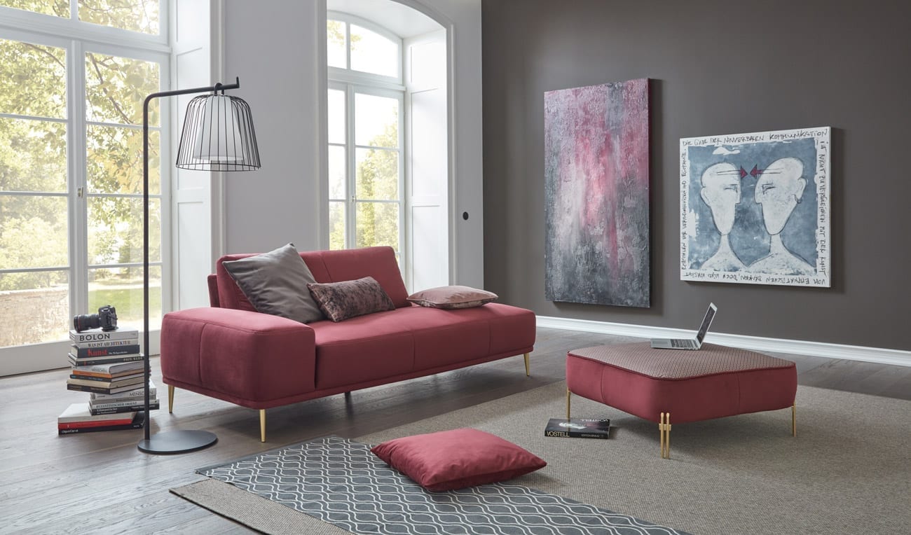 Wohnambiente mit einer Sofakombination des Modells Oslo mit rotem Stoffbezug, Wurfkissen, Nierenkissen, Reversekissen und goldigen Füssen
