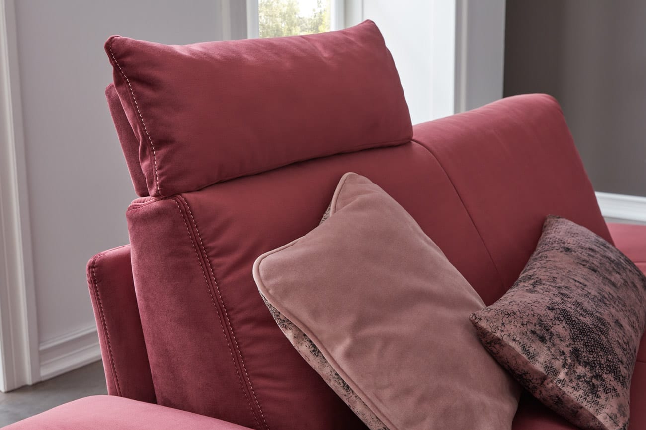 Wohnambiente mit einer Sofakombination des Modells Oslo mit rotem Stoffbezug, Kopfstütze, Reversekissen und Nierenkissen