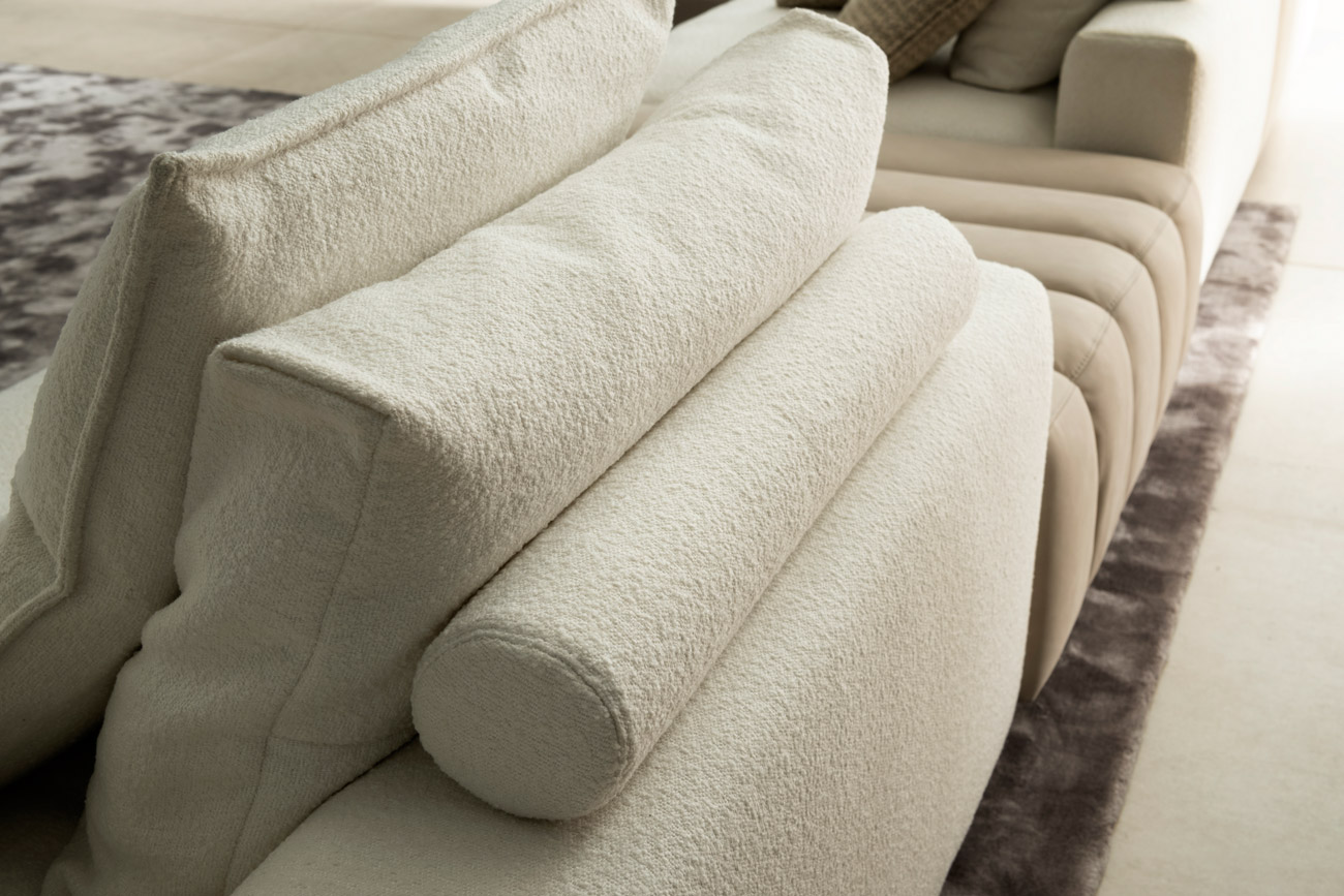 Wohnambiente mit einer Sofakombination des Modells Berry mit beigem Stoff-Lederbezug, Teppich Sense und Rückenkissen mit Rolle
