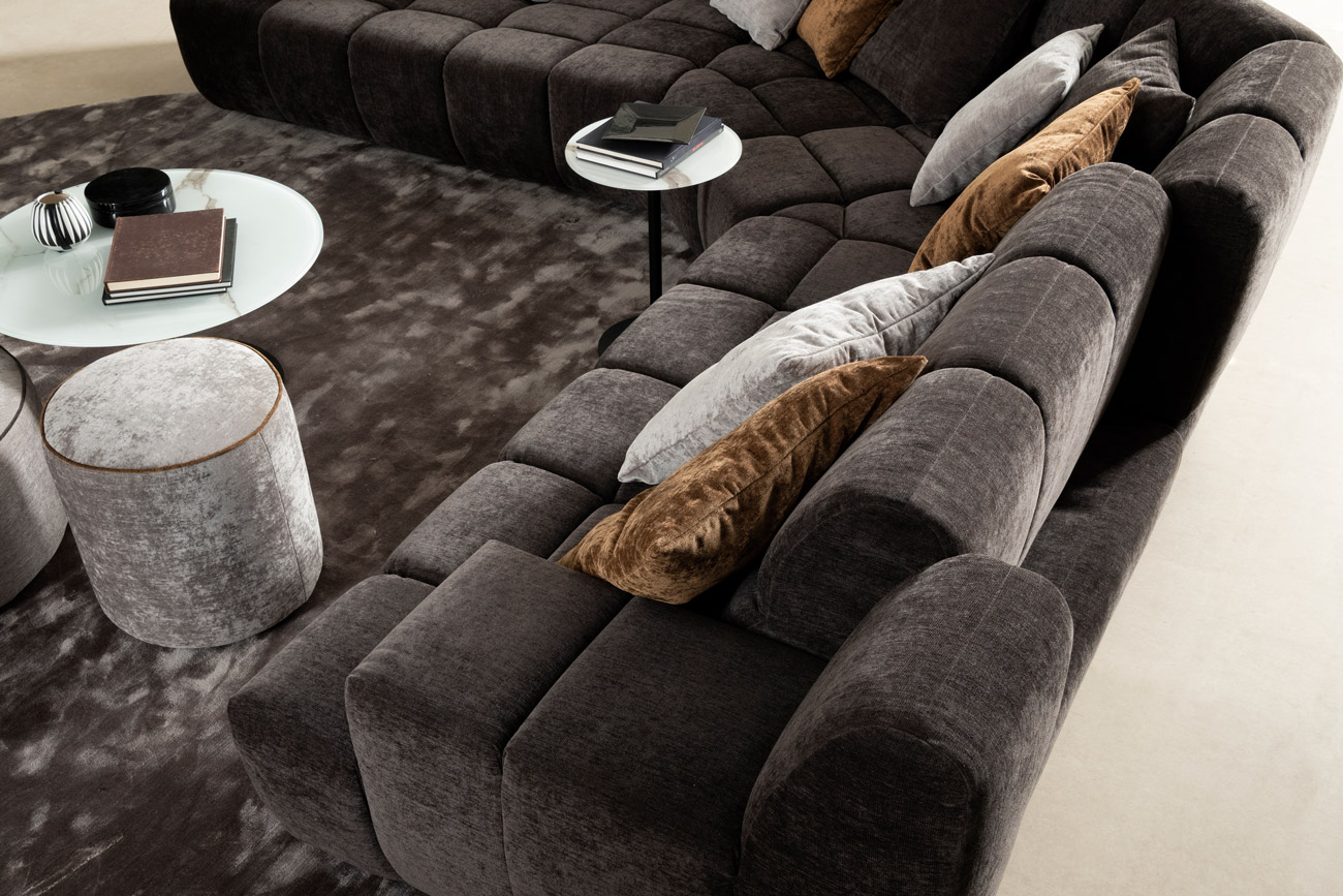 Wohnambiente mit einer Sofakombination des Modells Cielo mit braunem Stoffbezug, Wurfkissen, manueller Rückenverstellung, Hocker Rondo Mini, Center Leg und Teppich Sense