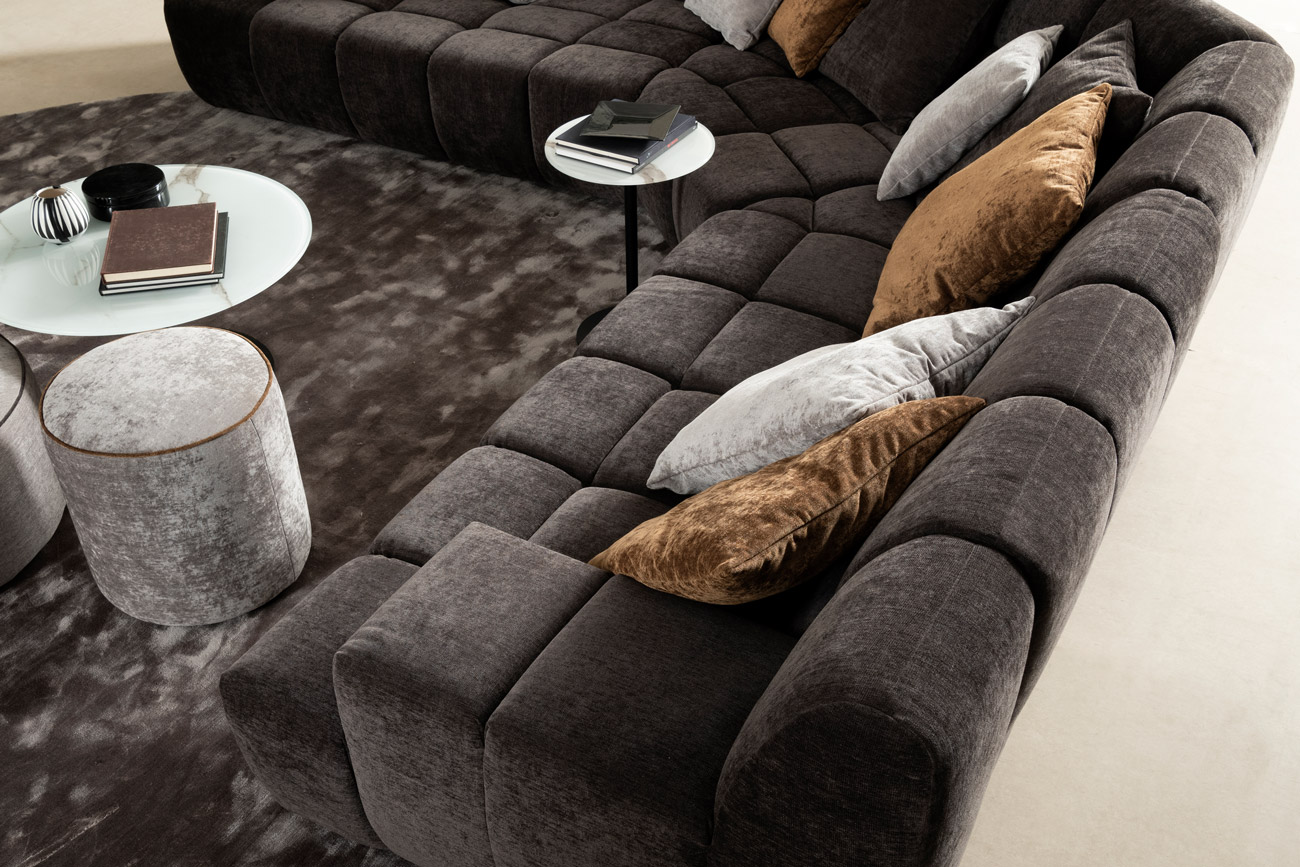 Wohnambiente mit einer Sofakombination des Modells Cielo mit braunem Stoffbezug, Wurfkissen, Hocker Rondo Mini, Center Leg und Teppich Sense