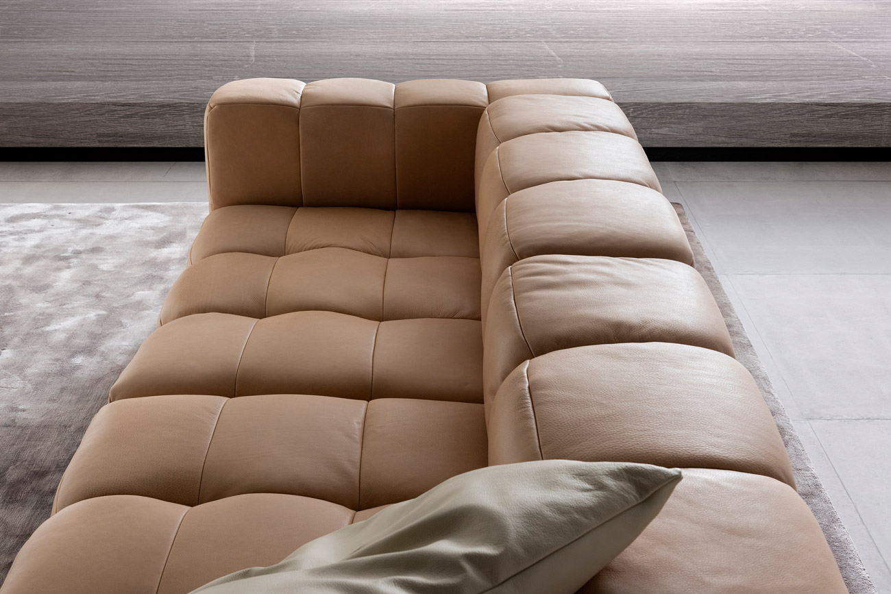 Wohnambiente mit einer Sofakombination des Modells Lucy mit beigem Lederbezug, Wurfkissen und Teppich Sense