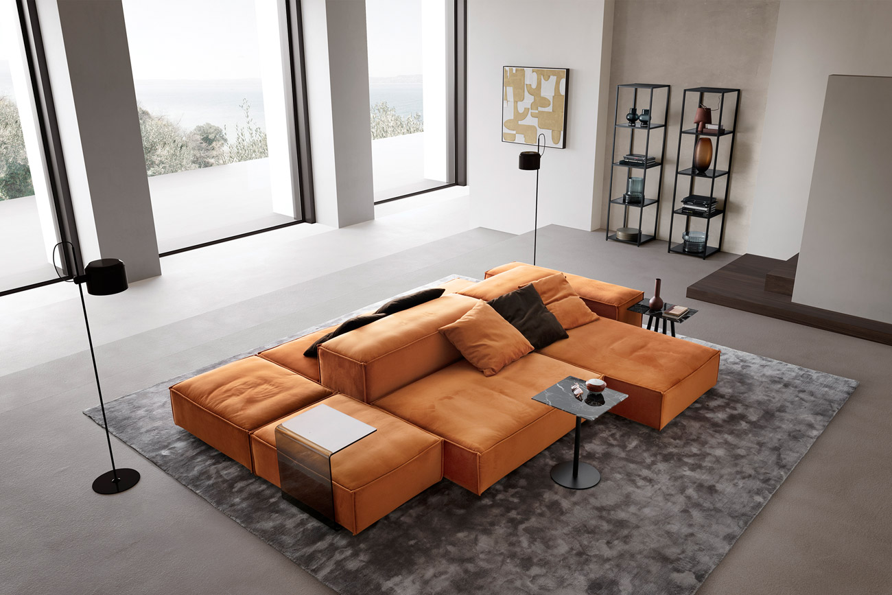 Wohnambiente mit einer Sofakombination des Modells Puzzle mit orangem Stoffbezug, Wurfkissen, C-Table, Center Leg, Four Leg, Tower und Teppich Sense