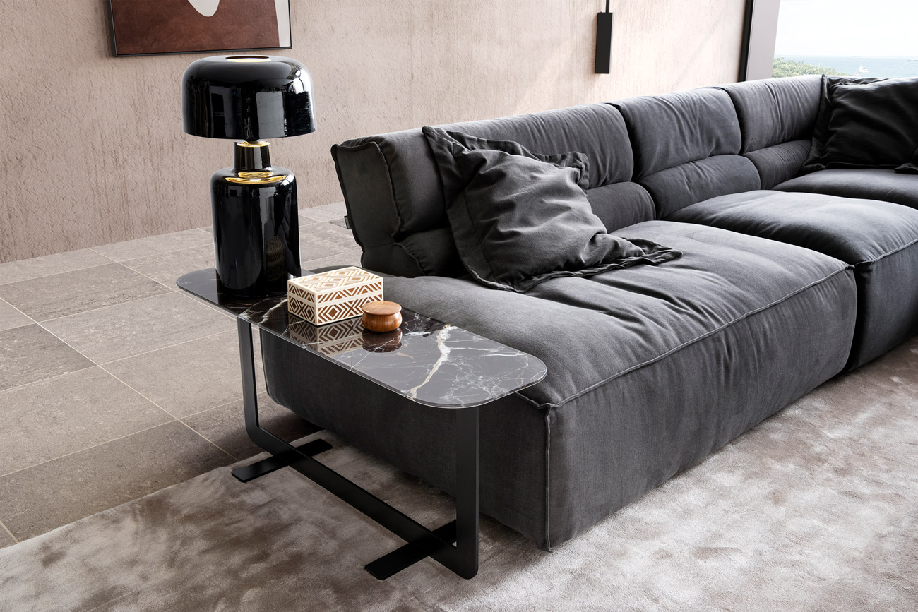 Wohnambiente mit einer Sofakombination des Modells Vola mit grauem Stoffbezug, Flatterkissen, One Blade und Teppich Sense