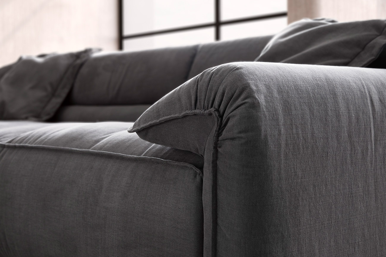 Wohnambiente mit einer Sofakombination des Modells Vola mit grauem Stoffbezug und Flatterkissen