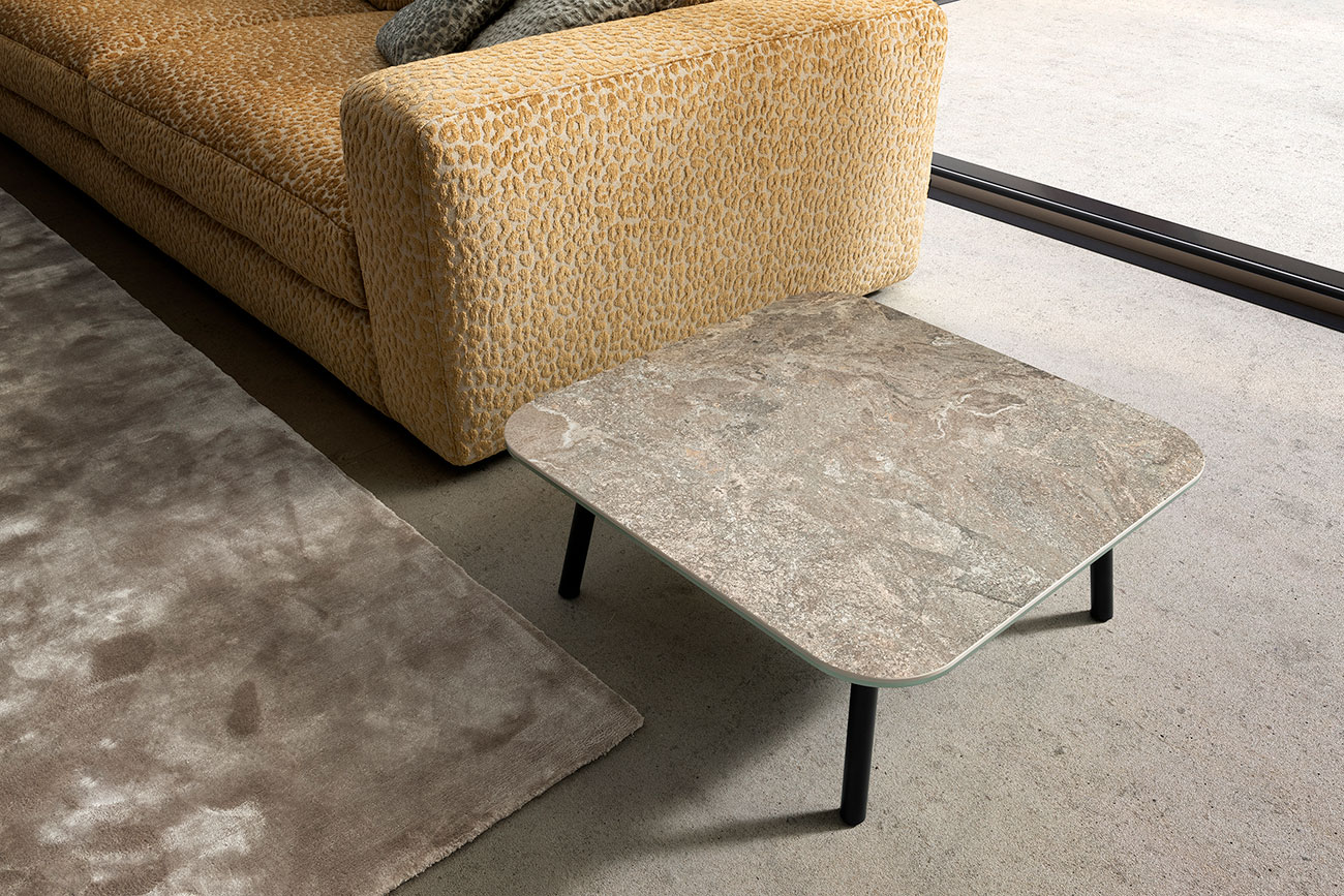 Wohnambiente mit Beimöbel Four Leg mit quadratischer Keramik-Platte Struttura Verde, Teppich Sense und Sofa Parma im Hintergrund